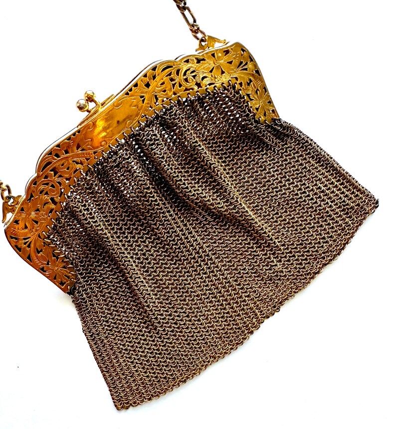 Pu&ograve; includere: Una borsa a catena dorata con una chiusura a filigrana e un corpo a rete.