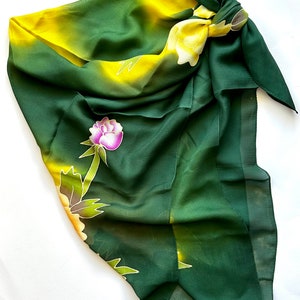 K&ouml;nnte beinhalten: Ein gr&uuml;ner und gelber Seidenschal mit einem Blumenmuster. Der Schal ist oben zu einem Knoten gebunden und hat einen Fransenrand.