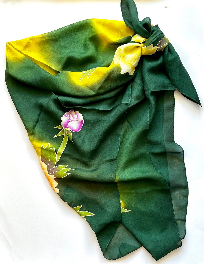K&ouml;nnte beinhalten: Ein gr&uuml;ner und gelber Seidenschal mit einem Blumenmuster. Der Schal ist oben zu einem Knoten gebunden und hat einen Fransenrand.