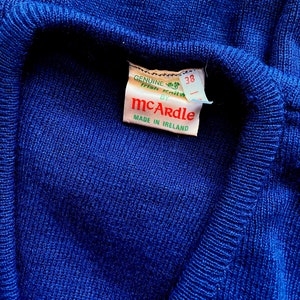 Może przedstawiać: Niebieski sweter z białym znaczkiem z napisem "GENUINE Irish Knitwear by McArdle MADE IN IRELAND" i metką rozmiaru z napisem "38".