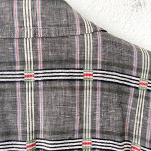 May include: A charcoal gray shirt featuring a textured weave with vertical pinstripes in white, blue, and red. The fabric is overlaid with horizontal bands of white and black stripes, accented by small squares containing red and green thread details.