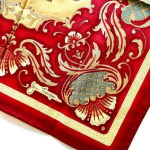 May include: A silk scarf with a vibrant red border and a central design featuring gold filigree and floral patterns. The scarf has a cream-colored background with an elephant illustration. The signature "Jim Thompson" is visible.