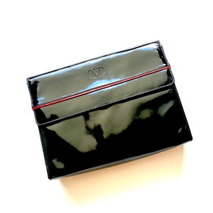 Op de afbeelding: Een zwarte clutch van gelakt leer met een rode bies en een reli&euml;f "VD" logo.