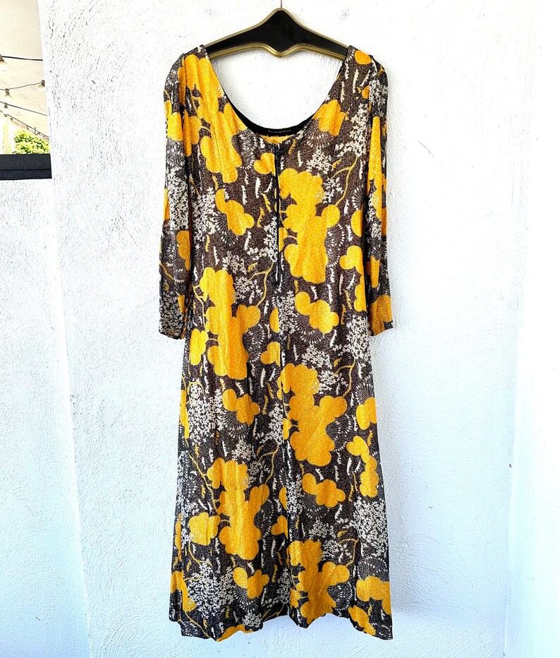 May include: A long, yellow and brown floral print dress with a scoop neck and long sleeves. The dress has a zipper closure in the back.