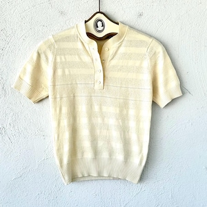 Pode incluir: Uma camisa de malha de manga curta de cor creme com colarinho de botões e um padrão listrado.