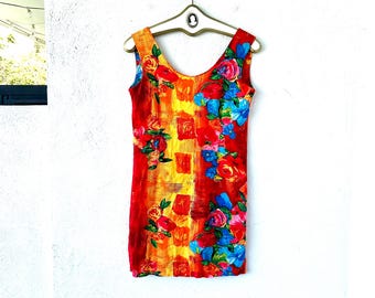 May include: Sleeveless dress with a vibrant floral print. The dress features a scoop neckline and a straight silhouette. The fabric is a mix of red, orange, and yellow with blue and pink floral accents. The dress is hanging on a vintage hanger.