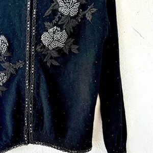Puede incluir: Su&eacute;ter negro con un dise&ntilde;o floral de cuentas en la parte delantera. El su&eacute;ter tiene manga larga y un borde de canal&eacute;.