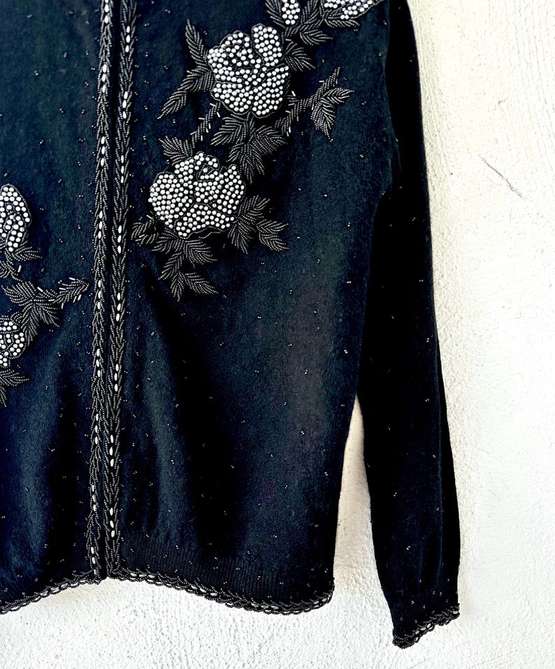 Puede incluir: Su&eacute;ter negro con un dise&ntilde;o floral de cuentas en la parte delantera. El su&eacute;ter tiene manga larga y un borde de canal&eacute;.
