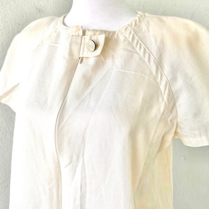 May include: A white short-sleeved button-up shirt with a round collar and a single button closure at the neckline.