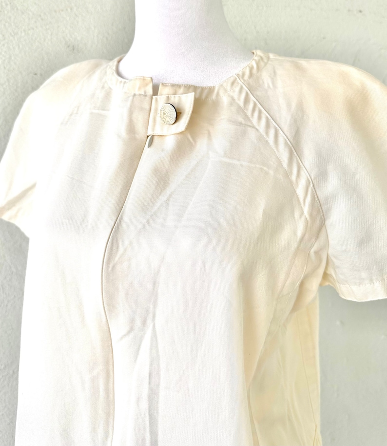 May include: A white short-sleeved button-up shirt with a round collar and a single button closure at the neckline.