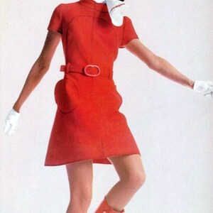 May include: A woman wearing a red mini dress with a white collar and a white scarf. She is wearing red boots and white gloves. The dress has a belt with a large buckle.