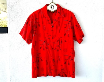 May include: A bright red short-sleeved shirt with a camp collar. The shirt features a black pattern of stylized bottles and palm trees. The shirt is buttoned and hanging on a white hanger against a white wall.