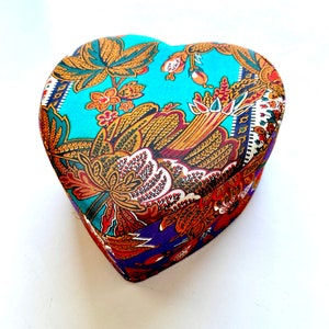 May include: A heart-shaped box with a colorful floral pattern. The box is made of fabric and has a blue, purple, and gold color scheme.