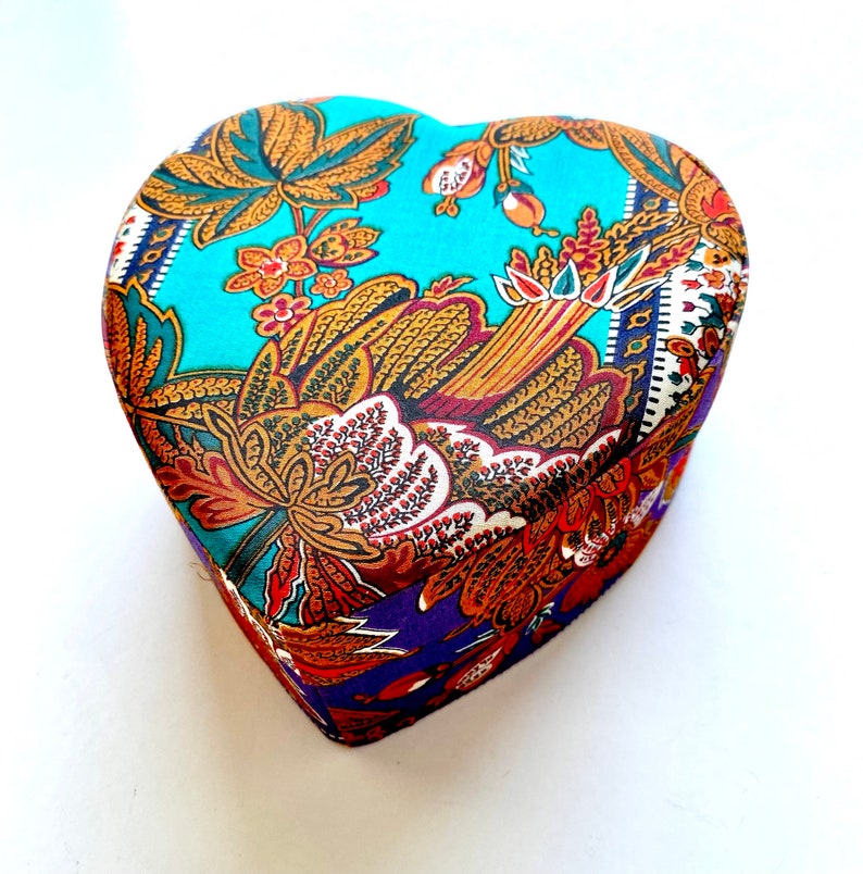 May include: A heart-shaped box with a colorful floral pattern. The box is made of fabric and has a blue, purple, and gold color scheme.