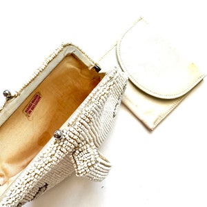 May include: A white beaded clutch purse with a matching white fabric pouch. The clutch has a metal clasp and a label that reads "Hand Made in Belgium".