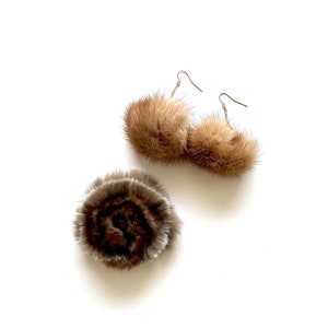May include: A pair of brown fur pom-pom earrings with gold hooks and a brown fur pom-pom brooch.