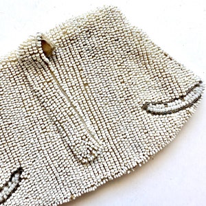 May include: A white beaded clutch purse with a zipper closure. The purse is made of small, round beads that are sewn together in a tight pattern.