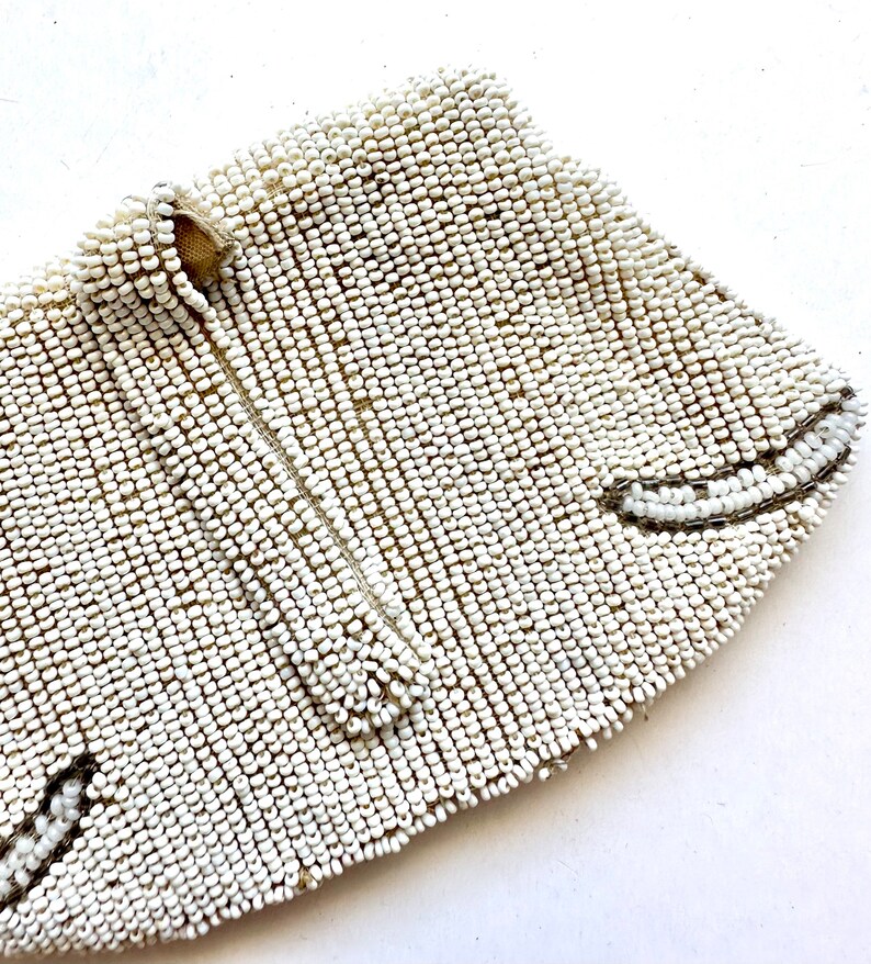 May include: A white beaded clutch purse with a zipper closure. The purse is made of small, round beads that are sewn together in a tight pattern.