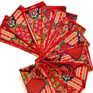 Puede incluir: Un conjunto de servilletas de tela rojas dispuestas en forma de abanico. Cada servilleta presenta un vibrante estampado de cachemir y floral en verde, azul, amarillo y blanco. Las servilletas tienen un borde rojo sobre fondo blanco.
