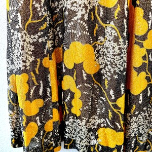 May include: Close-up of a black and gold fabric with a floral pattern. The fabric has a shimmery texture and features a repeating design of stylized flowers and leaves.