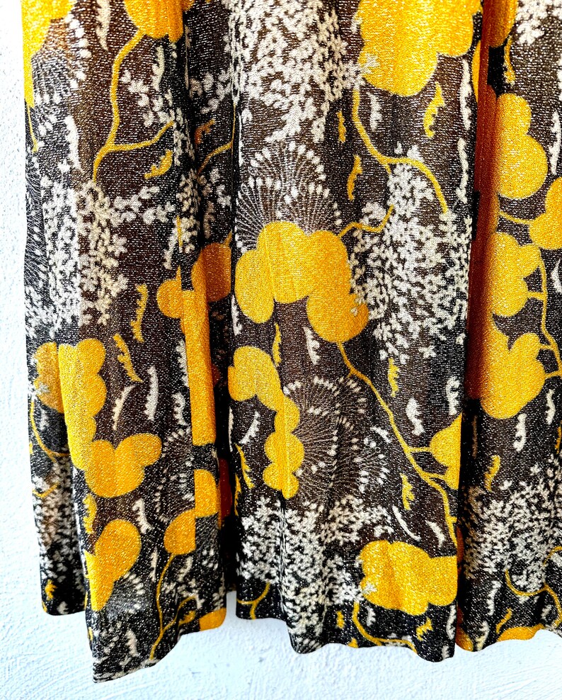 May include: Close-up of a black and gold fabric with a floral pattern. The fabric has a shimmery texture and features a repeating design of stylized flowers and leaves.