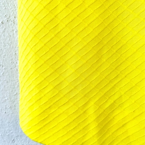 Pu&ograve; includere: Primo piano di un tessuto giallo brillante con un motivo a rombi testurizzato.