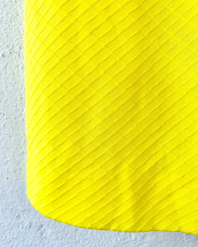 Pu&ograve; includere: Primo piano di un tessuto giallo brillante con un motivo a rombi testurizzato.