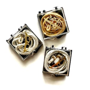 May include: Three small clear plastic boxes with black lids containing gold and silver cords with gold accents.