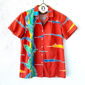 May include: A red short-sleeved button-down shirt with a colorful tropical print. The print features palm trees and a rainbow stripe on the left side of the shirt.