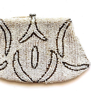 May include: A white beaded clutch purse with a silver clasp. The purse has a geometric design with a repeating pattern of curved lines.