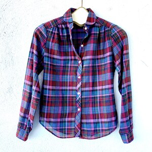 May include: A long-sleeved plaid shirt with a button-up front. The shirt is a mix of purple, blue, and red plaid.