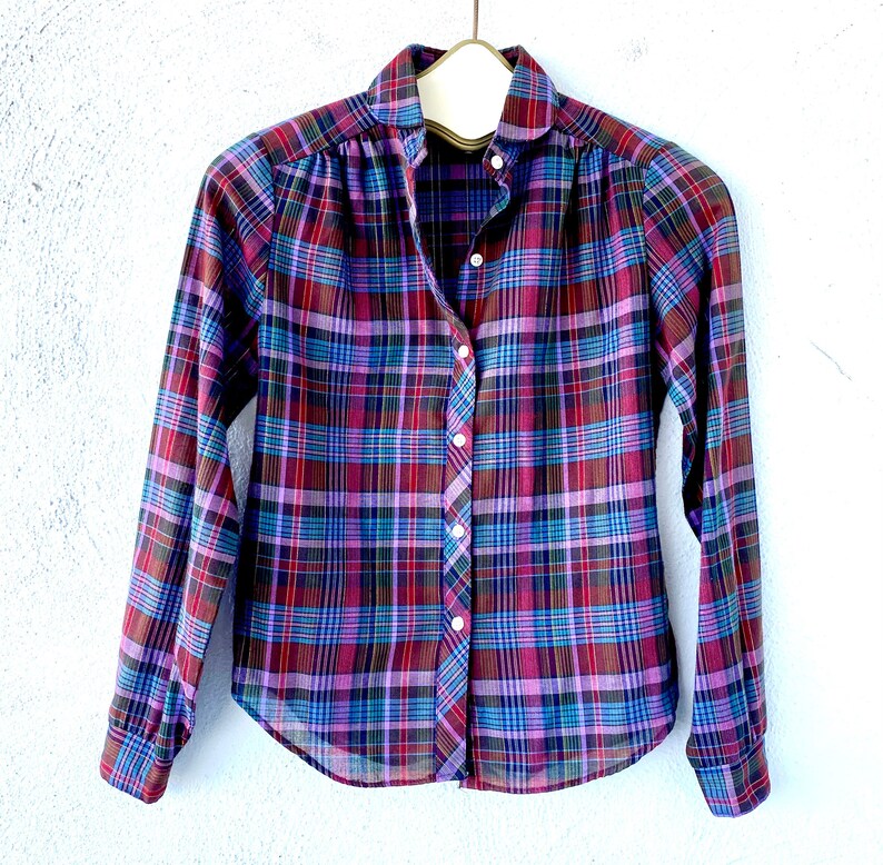 May include: A long-sleeved plaid shirt with a button-up front. The shirt is a mix of purple, blue, and red plaid.