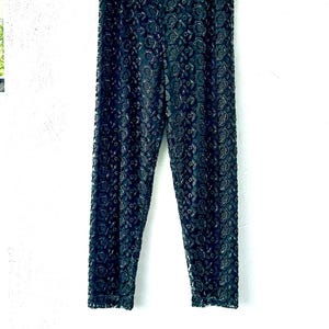 May include: A pair of black trousers featuring an intricate, all-over floral lace pattern. The pants have a straight-leg silhouette with a consistent dark color throughout, showcasing a detailed, textured fabric design that covers the entire garment.