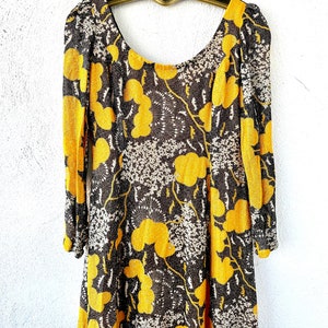 May include: A long-sleeved dress with a scoop neck and a brown and yellow floral print. The dress is made of a sheer fabric and has a loose fit.