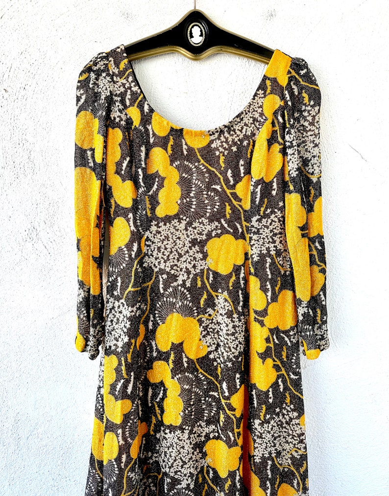 May include: A long-sleeved dress with a scoop neck and a brown and yellow floral print. The dress is made of a sheer fabric and has a loose fit.