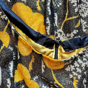 May include: Close-up of a black and gold fabric with a floral pattern. The fabric has a zipper and a black trim.