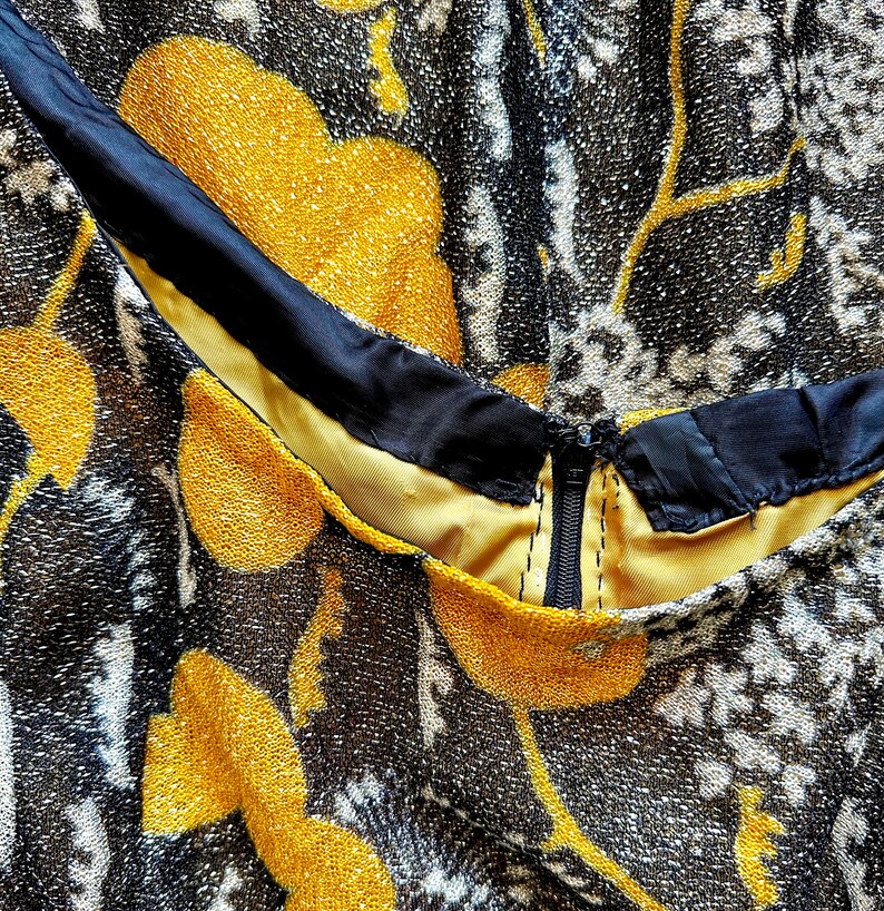 May include: Close-up of a black and gold fabric with a floral pattern. The fabric has a zipper and a black trim.