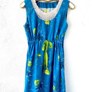 May include: A blue sleeveless dress with a white crochet neckline and a green ribbon tie at the waist. The dress has a floral print with yellow and green flowers.