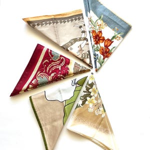 May include: An overhead shot of five folded silk scarves. The scarves feature various patterns, including floral, paisley, and elephant motifs. Colors include red, beige, white, green, and blue. The scarves are arranged in a starburst pattern against a white background.