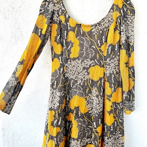 May include: A long-sleeved dress with a scoop neck and a floral print. The dress is made of a sheer fabric with a yellow and brown pattern.