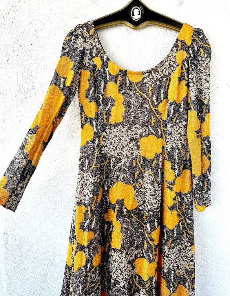 May include: A long-sleeved dress with a scoop neck and a floral print. The dress is made of a sheer fabric with a yellow and brown pattern.