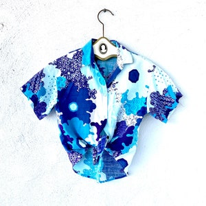 May include: A white, blue, and purple short-sleeved button-up shirt with a floral pattern. The shirt is tied at the waist.