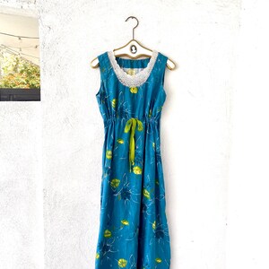 May include: A blue maxi dress with a white crochet neckline and green ribbon tie. The dress has a floral print with yellow and green flowers.