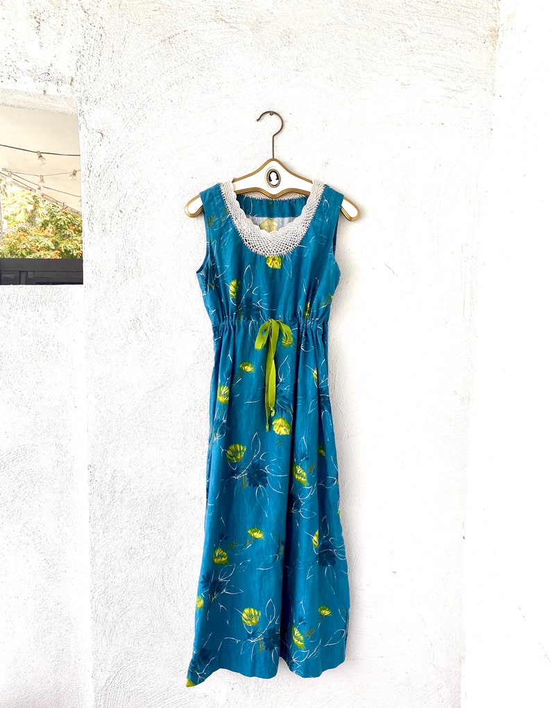 May include: A blue maxi dress with a white crochet neckline and green ribbon tie. The dress has a floral print with yellow and green flowers.