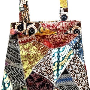 May include: A patchwork tote bag with a variety of patterned fabric pieces in shades of brown, red, blue, and yellow. The bag has two straps and a rectangular shape, perfect for carrying items.