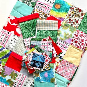 May include: A colourful patchwork quilt made from various patterned fabrics. The quilt incorporates squares of red, green, blue, and yellow materials with floral, geometric, and animal designs. A collection of fabric scraps is placed on top of the quilt.