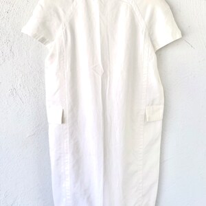 May include: A white linen dress with short sleeves and a round neckline. The dress has a simple design with a straight silhouette and a slightly flared skirt.