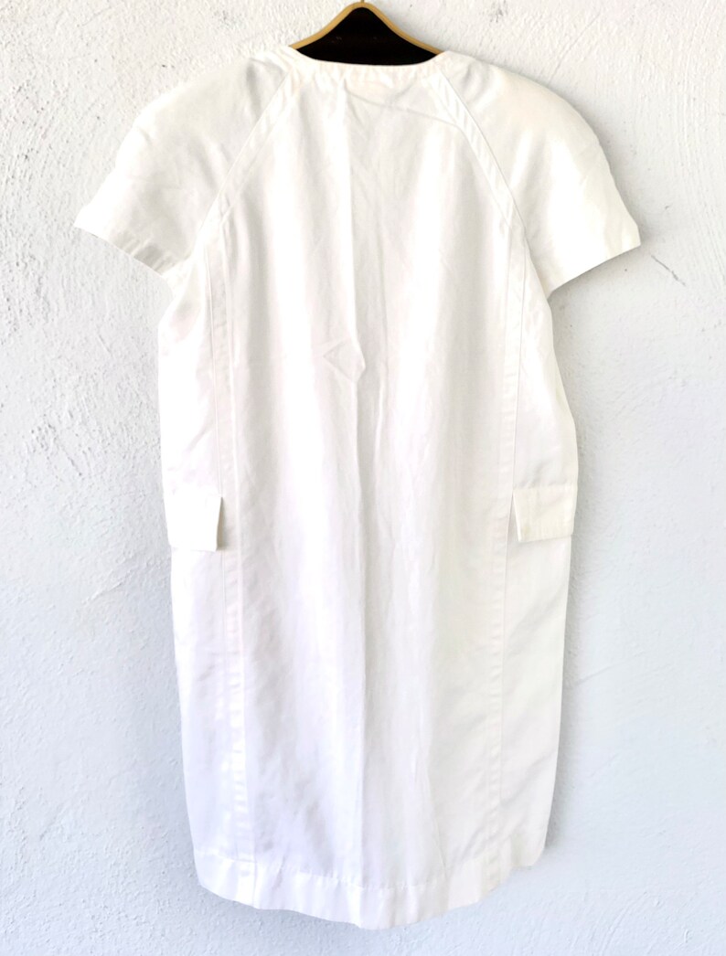 May include: A white linen dress with short sleeves and a round neckline. The dress has a simple design with a straight silhouette and a slightly flared skirt.
