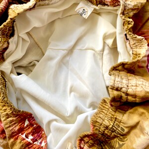 May include: Close-up of a pair of shorts with a floral pattern in shades of brown, red, and gold. The shorts have an elastic waistband and a white lining. A tag with the word "Troy" is visible.