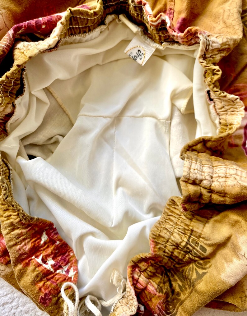 May include: Close-up of a pair of shorts with a floral pattern in shades of brown, red, and gold. The shorts have an elastic waistband and a white lining. A tag with the word "Troy" is visible.